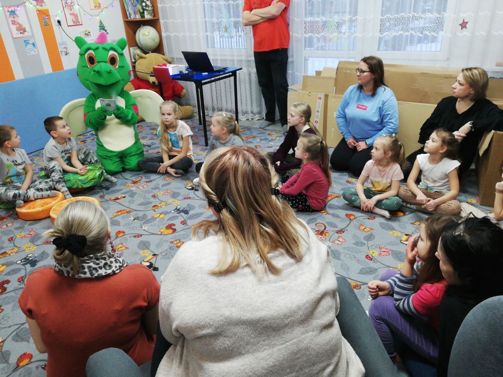 Dzieci i rodzice słuchają Smoczycy - bibliotecznej maskotki, która odwiedziła dzieci na zajęciach.