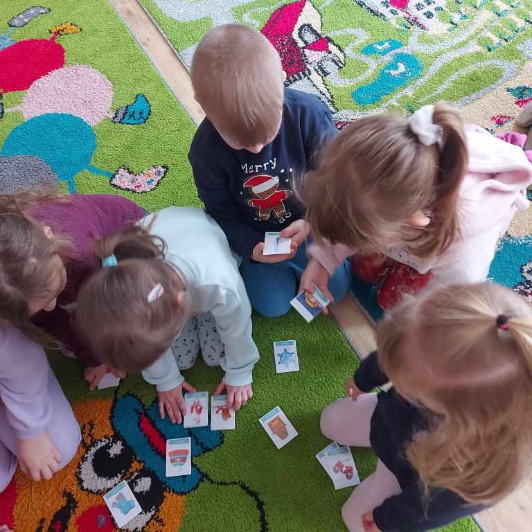 Dzieci pochylają się nad rozsypanymi między nimi kartami do gry.