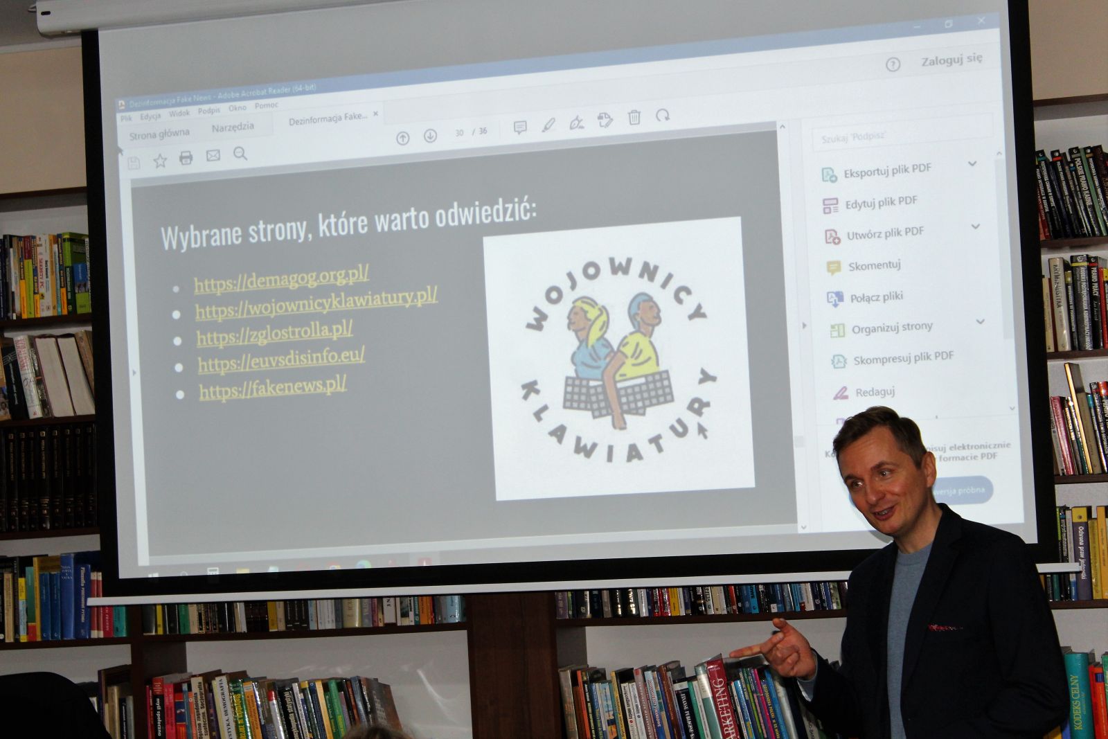Na zdjęciu prowadzący wykład Dominik Sołowiej na tle prezentacji wyświetlanej na rozwiniętym ekranie.