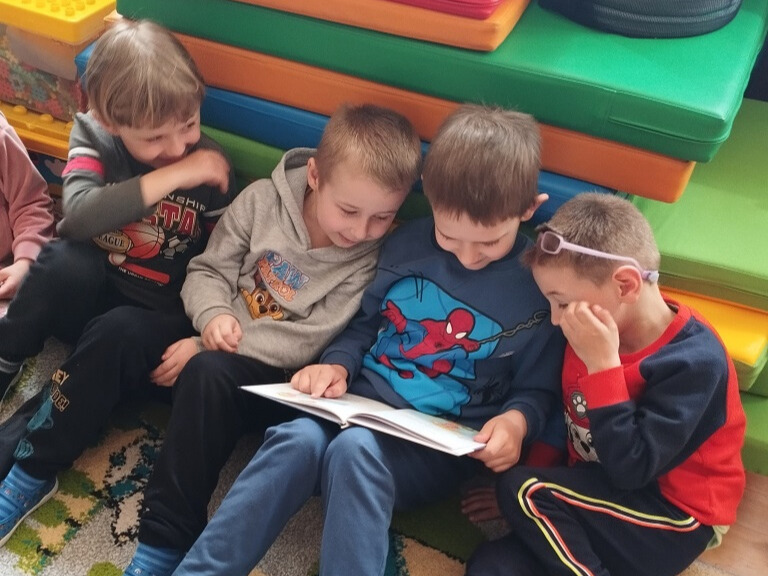 Trzech chłopców czyta wspólnie jedną książkę.